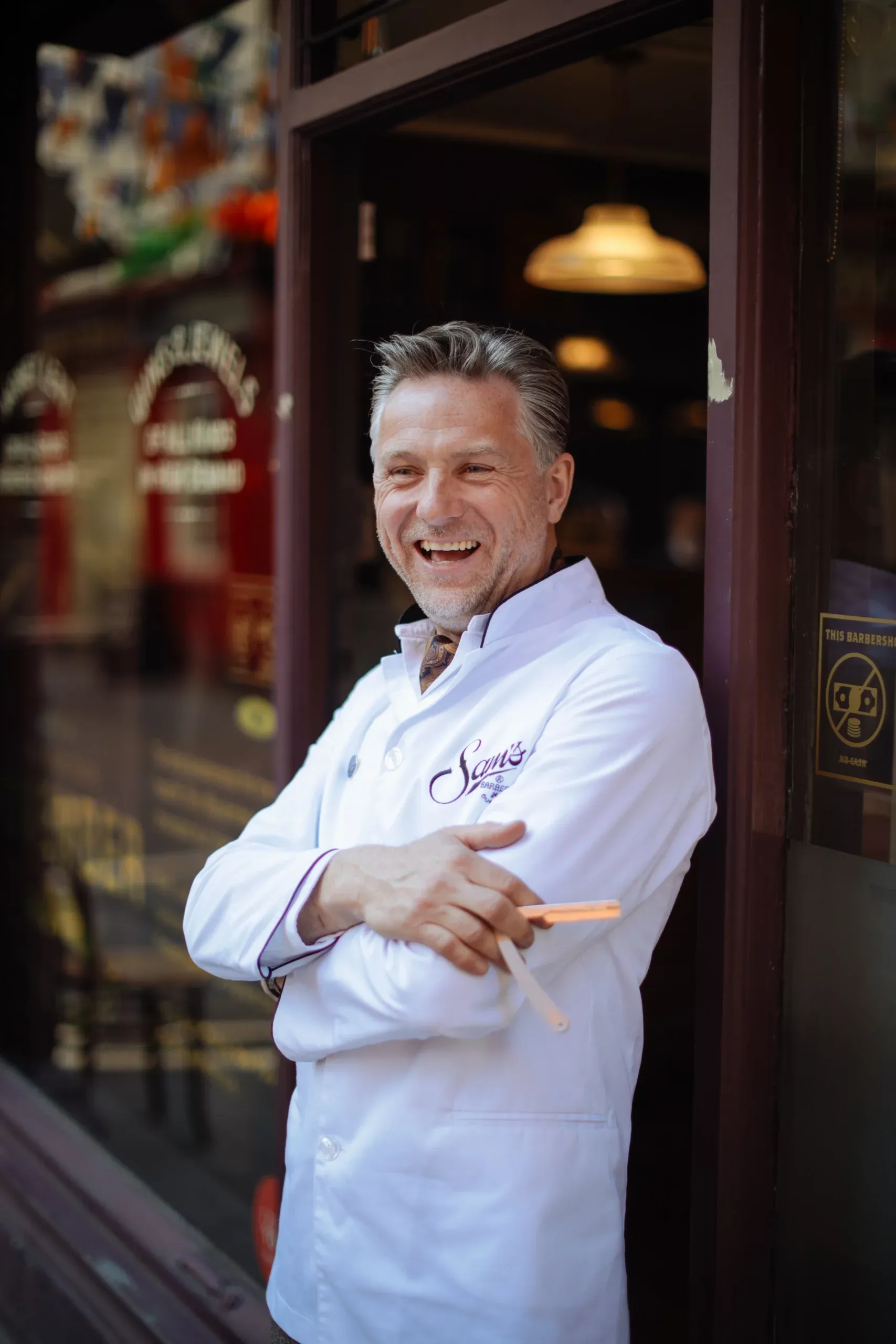 A Sam's barber smiling in a shop doorway